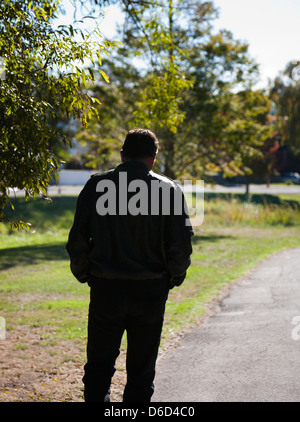 Back view of a man, deep in thought, walking alone along a path, silhouetted against a rural setting. Stock Photo