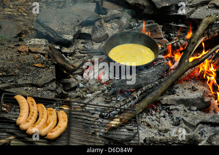 Fried eggs on fire at iron fried pan with grilled sausages on skewer Stock Photo