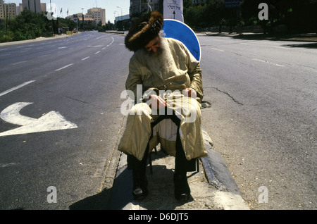 An Ultra Orthodox Jew wearing a shtreimel fur hat sits chained to a traffic sign so he can 'suffer' seeing cars driving on Saturday or Shabbat, the Jewish day of rest and seventh day of the week in West Jerusalem Israel Stock Photo