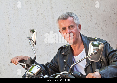 Capture of a Caucasian motorbiker in casual attire and relaxed expression looking into lens sat on a red cruiser. Stock Photo