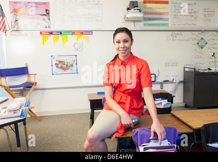 Mixed race teacher sitting on desk in classroom Stock Photo