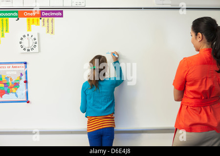 Teacher watching student write on whiteboard in classroom Stock Photo