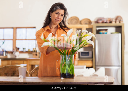 Older Hispanic woman arranging flowers in kitchen Stock Photo