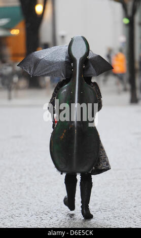 A young woman carries her double bass on her back and tries to protect herself from the pouring rain with an umbrella while walking across Potsdamer Platz in Berlin, Germany, 19 January 2012. Photo: Jens Kalaene