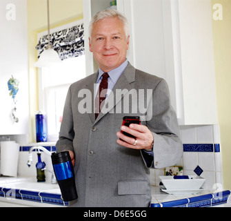 Businessman using cell phone in kitchen Stock Photo