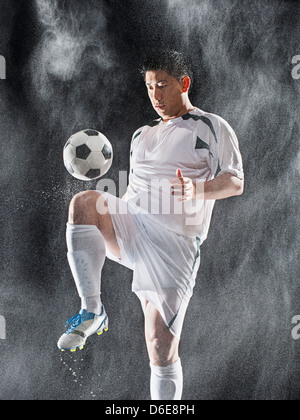 Asian soccer player kicking ball in rain Stock Photo