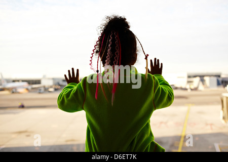Mixed race girl looking out airport window Stock Photo
