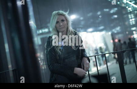 Pretty blonde young woman leaning on metal railings, alone in a city at night. Stock Photo