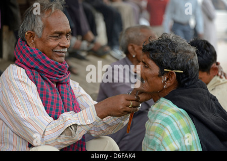 A barber giving his customer a wet shave amongst a row of squatting barbers in a street in Old Delhi, India. Stock Photo