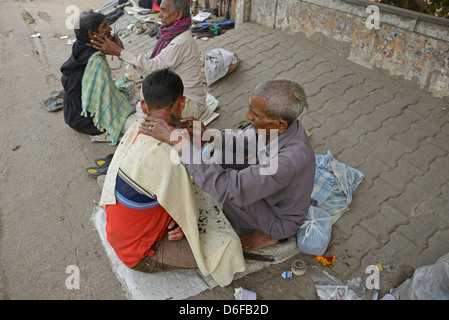 A barber giving his customer a wet shave amongst a row of squatting barbers in a street in Old Delhi, India. Stock Photo