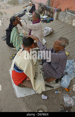 A barber giving his customer a wet shave amongst a row of squatting barbers in a street in Old Delhi, India. Stock Photo