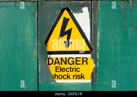 An old  and peeling "Danger Electric shock risk" sign on a painted green background in Bristol, U.K.. Stock Photo