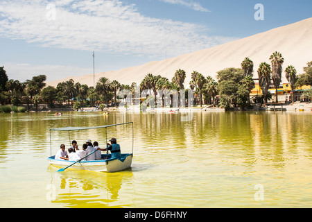 Man rowing a boat with children in the lagoon of Huacachina Oasis. Ica, Department of Ica, Peru. Stock Photo