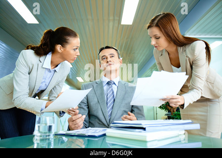 Inspirated boss sitting at workplace surrounded by two secretaries with papers Stock Photo