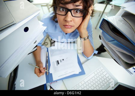 Perplexed accountant doing financial reports surrounded by huge piles of documents Stock Photo