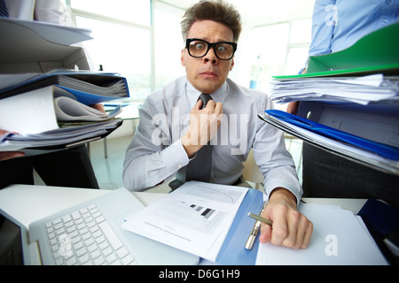 Shocked accountant looking at camera surrounded by huge piles of documents held by his partners Stock Photo