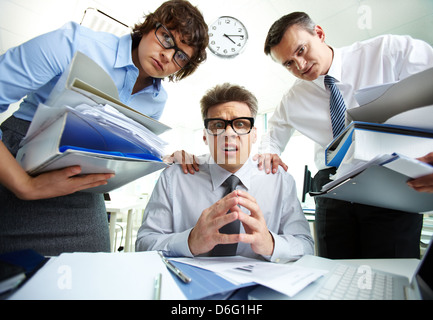 Pleading accountant looking at camera being surrounded by his partners with huge piles of documents Stock Photo