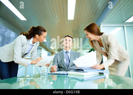 Inspirated boss sitting at workplace surrounded by two secretaries Stock Photo