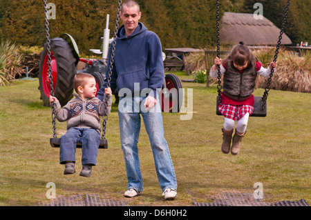 Parent Pushing His Children On Swings Stock Photo