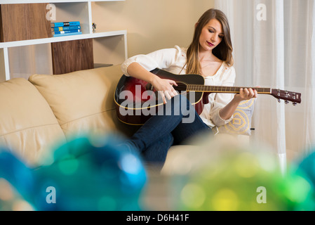 Woman playing guitar on sofa Stock Photo