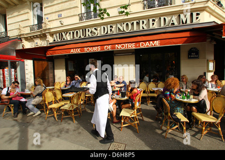 People enjoying first spring sun at sidewalk cafe next to Notre Dame cathedral in central Paris, France. Stock Photo