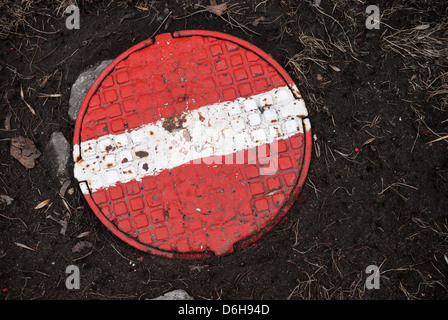 Round steel sewer manhole with painted red stop sign on it Stock Photo