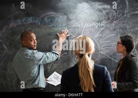Man writing on blackboard, colleagues watching Stock Photo