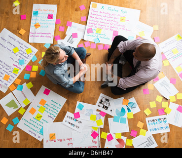 Colleagues sitting cross legged on floor with papers and adhesive notes Stock Photo
