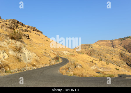 A curved black empty road running through yellow hills, covered with withered grass Stock Photo
