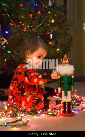 Twenty Month Old Boy Playing with Nutcracker beside Christmas Tree Stock Photo