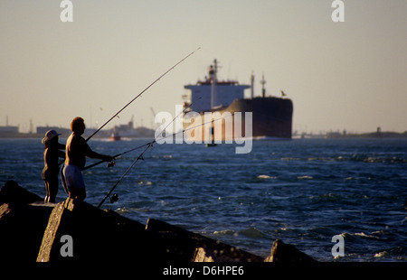 Man and woman fishing on the jetties at Port Aransas Texas while an oil tanker ship approaches Stock Photo