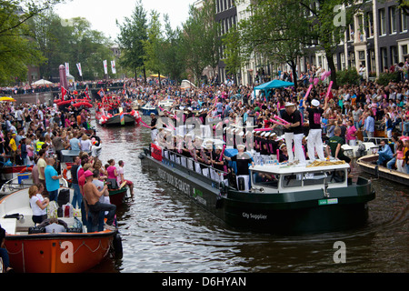 The Gay Pride Parade down a crowded canal lined with people and boats in Amsterdam, Holland. Stock Photo