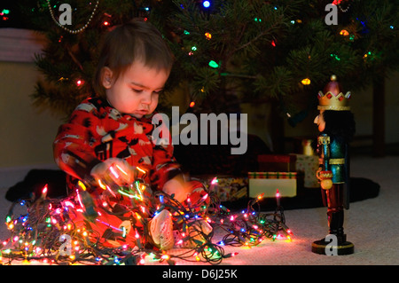 Twenty Month Old Boy Playing with Nutcracker beside Christmas Tree Stock Photo