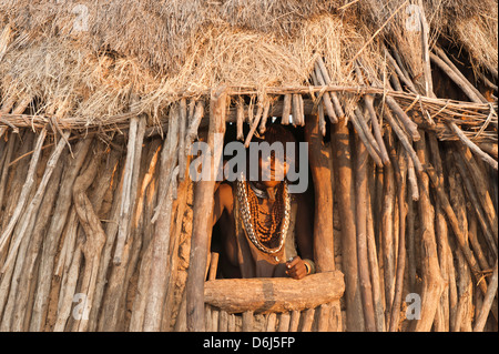 Pregnant Hamar woman with necklaces made of cowry shells coming out of her wooden hut, Omo River Valley, Southern Ethiopia Stock Photo