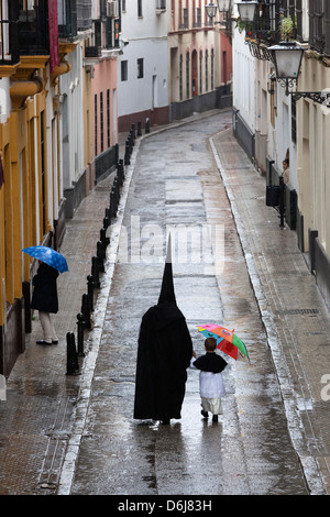 Penitents during Semana Santa (Holy Week) along rainy street, Seville, Andalucia, Spain, Europe Stock Photo
