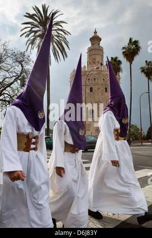 Penitents during Semana Santa (Holy Week) beneath Torre del Oro, Seville, Andalucia, Spain, Europe Stock Photo