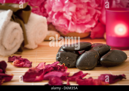 Massage stones with pink peony flowers, candles and towels. Aromatherapy spa scene. Stock Photo