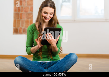 Online Dating - young woman sitting at home on the floor and buying new furniture over the Internet using a tablet computer Stock Photo