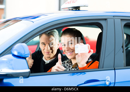 Driving School - Young woman steer a car, maybe she has a driving test, she holding proudly her driving license Stock Photo