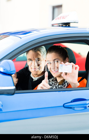 Driving School - Young woman steer a car, maybe she has a driving test, she holding proudly her driving license Stock Photo