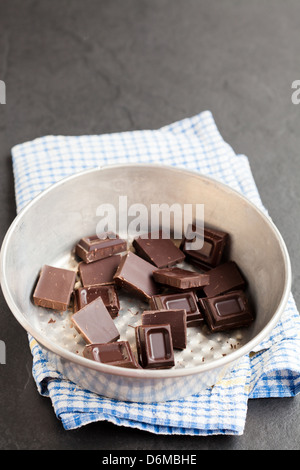 Closeup of bowl containing pieces of chocolate resting on blue checkered napkin on dark background Stock Photo