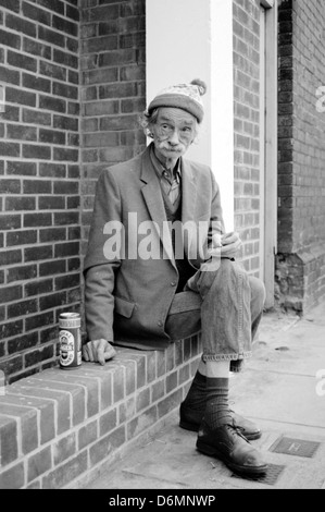 homeless man sitting in street smoking and drinking can of beer Stock Photo