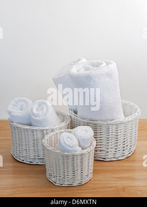 Clean towels in white wicker baskets, on a wooden surface. Stock Photo