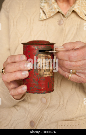 Elderly woman putting fifty pence into battered savings tin Stock Photo