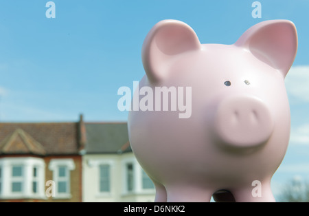 Pink piggy bank with row of houses in the background against a blue sky. Stock Photo