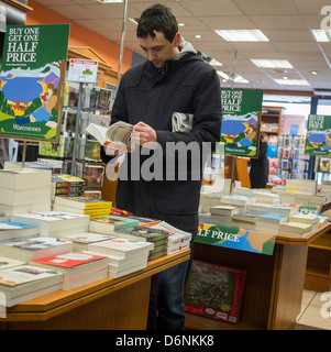 A man reading a book in the 'Buy One Get One Half Price' section of a branch of Waterstones bookshop, UK Stock Photo