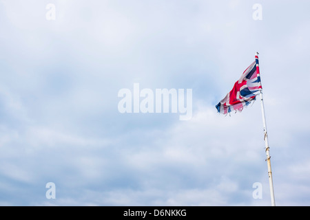 a tattered union jack flag banner flying on an overcast day, UK Stock Photo