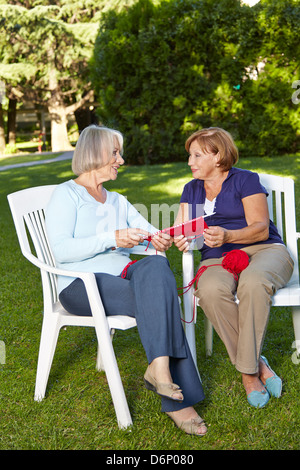 Two senior women knitting a scarf together in a summer garden Stock Photo