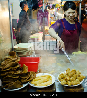Beautiful girl preparing food at one of many stands on a food market, Taiwan. Stock Photo