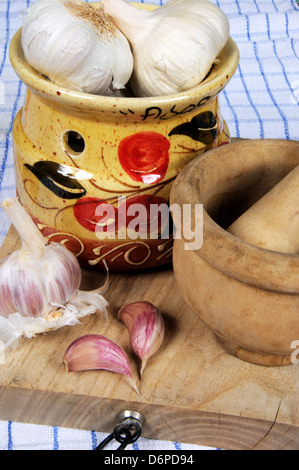 Ceramic garlic pot, garlic bulbs and pestle and mortar on a wooden chopping board. Stock Photo